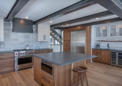 This kitchen has gorgeous warm wood cabinets and flooring, steel beams on the ceiling, and a calming gray backsplash that complements stainless fixtures.
