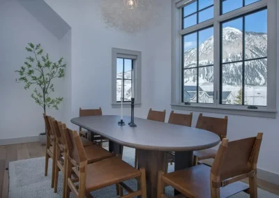 A cheerful dining room reflects warm brown tones in the furniture, white walls, gray trim, while an incredible view of Mt. Crested Butte is perfectly framed in large windows.